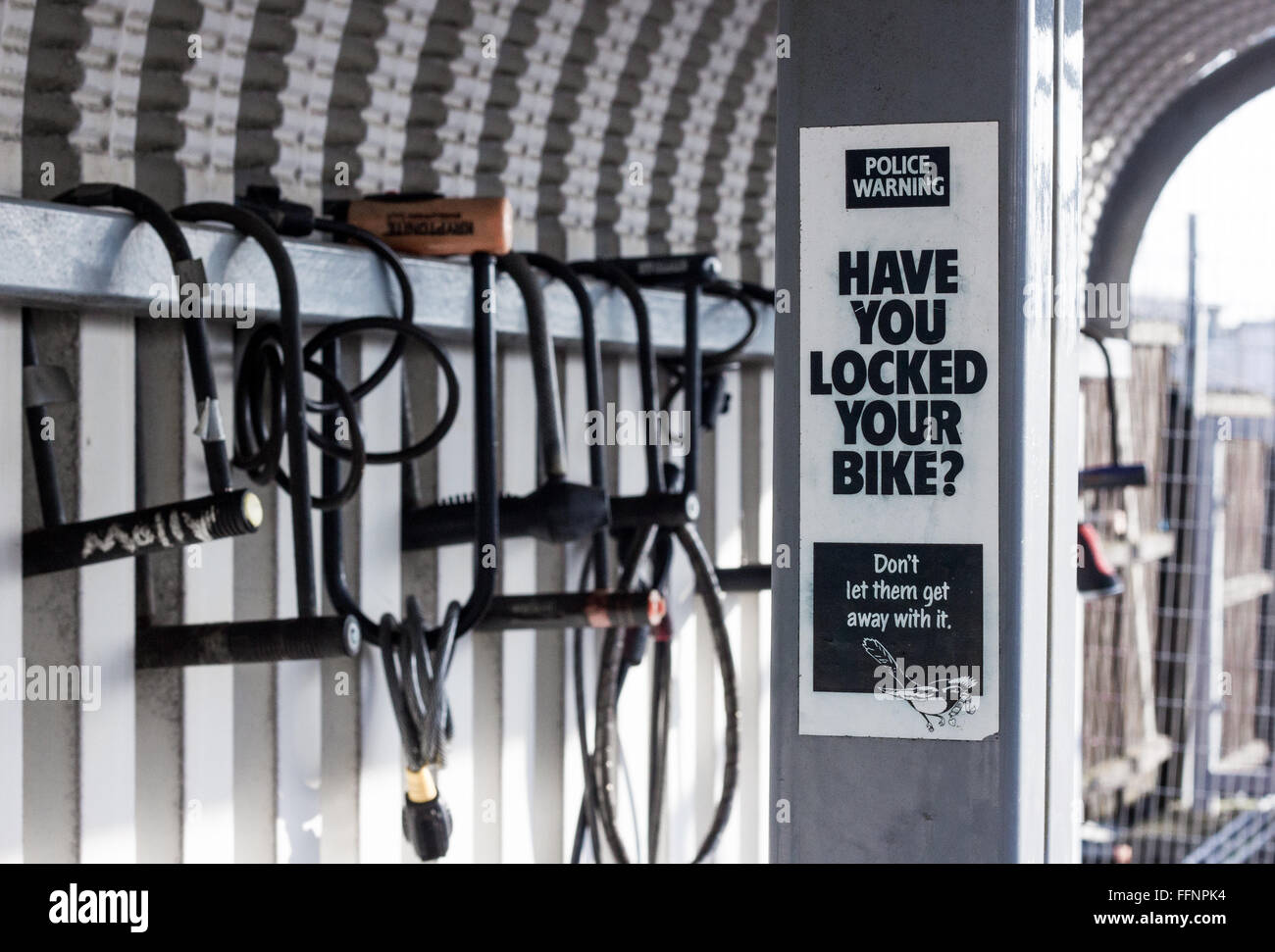 Ein "Haben Sie Ihr Fahrrad gesperrt?" Schild Warnung vor Fahrraddiebstahl vor Fahrradschlösser gesperrt um eine Fahrrad-Unterstand mit keine Fahrräder. Stockfoto