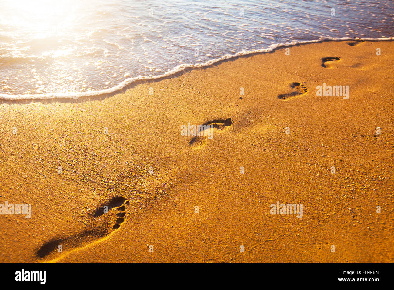 Strand, Wellen und Fußabdrücke bei Sonnenuntergang Stockfoto