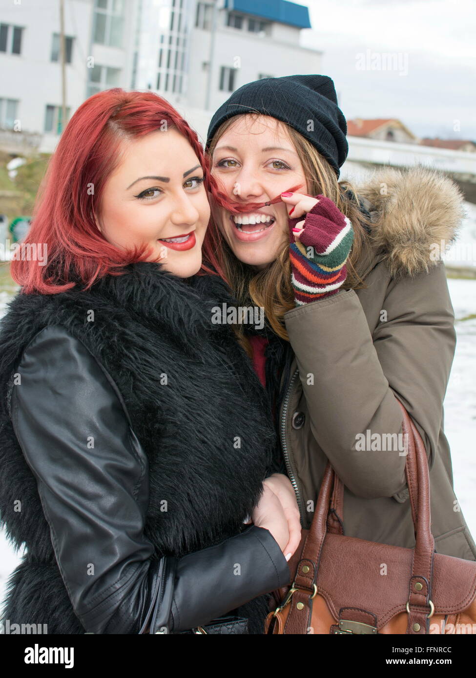 zwei Mädchen, die Spaß in das Winterwetter, ist ein Mädchen einen Schnurrbart mit ihren Haaren machen. Stockfoto