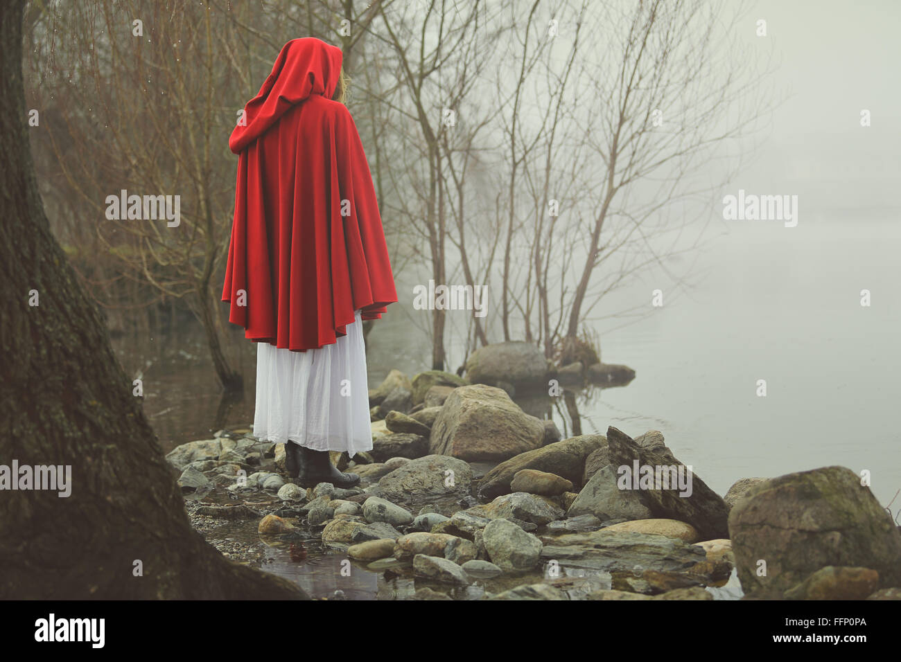 Kleine rote Reiten Haube an einem Ufer eines nebligen Sees. Traurigkeit und surreale Konzept Stockfoto