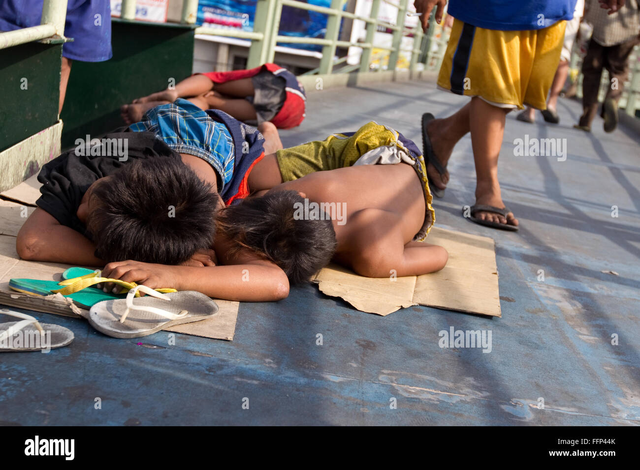 Straßenkinder schlafen auf Pappe auf einer Fußgängerüberführung in Pasay, Manila, während Pendler vorbeifahren, was die Armut in der Stadt und die harte Lebensrealität hervorhebt. Stockfoto