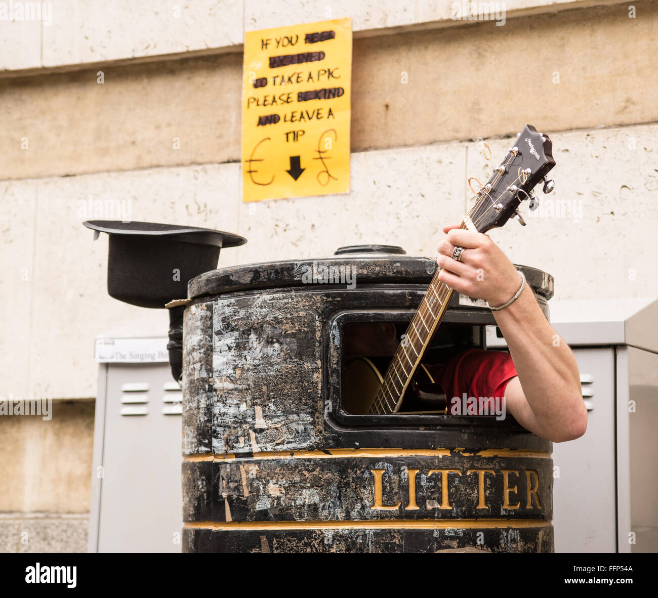 Busker singen und Gitarre spielen in einem Mülleimer an einer Straße. Stockfoto