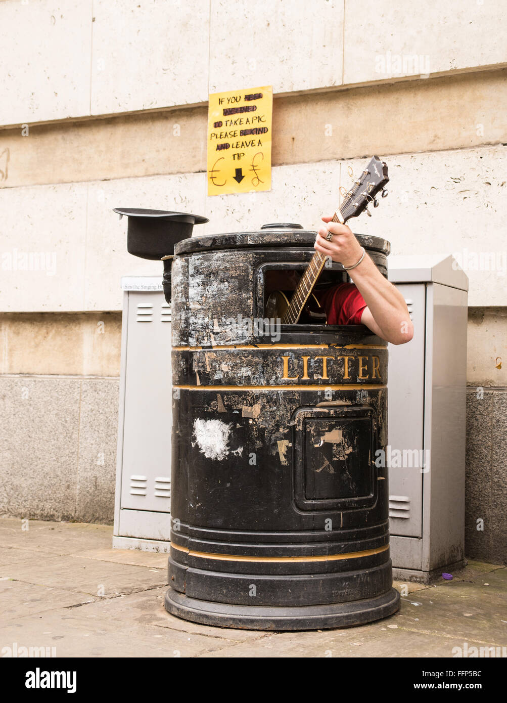 Busker singen und Gitarre spielen in einem Mülleimer an einer Straße. Stockfoto