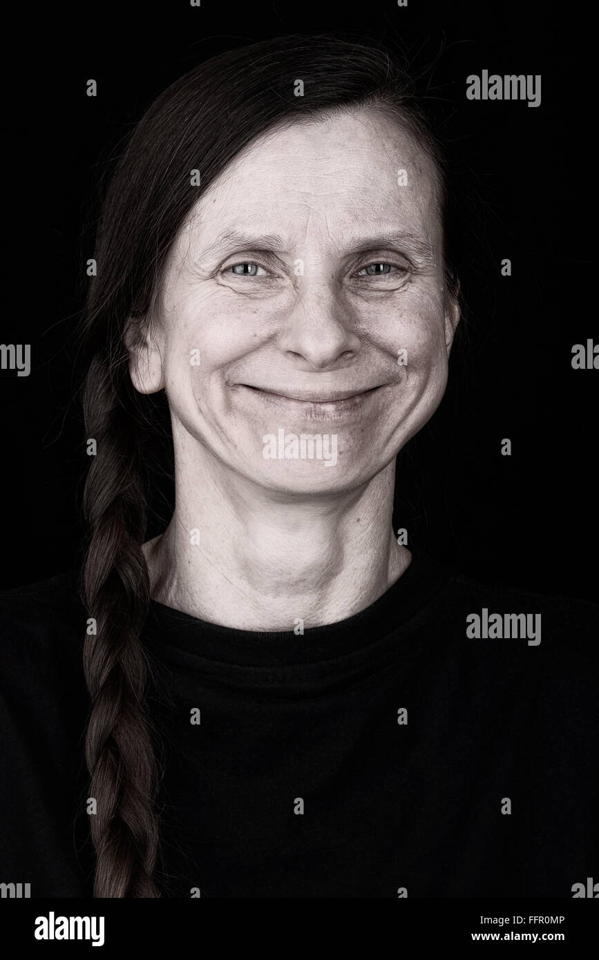 Eine glückliche Erwachsene Frau mit einem langen Zopf lächelt mit einem warmen und positiven Ausdruck Stockfoto