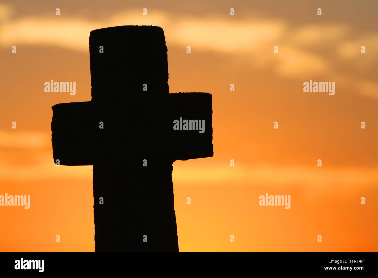 Ein verwitterten Stein christliches Kreuz gegen einen orange Sonnenuntergang. Stockfoto