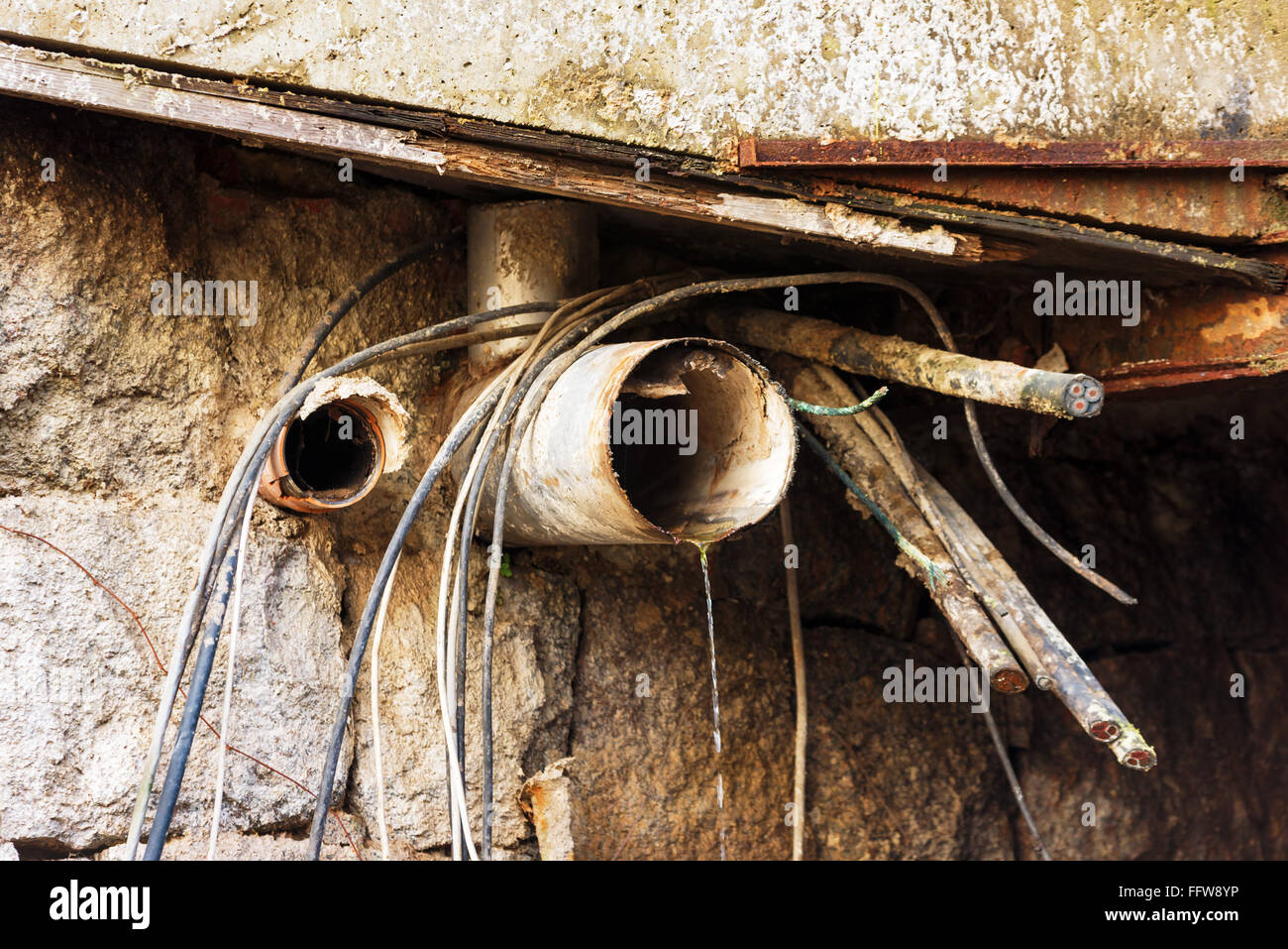 Alten Abflussrohre und geschnittenen elektrische Leitungen aus den unter Ruinen eines alten Fabrikgebäudes. Eine kleine Menge Wasser rieseln Stockfoto