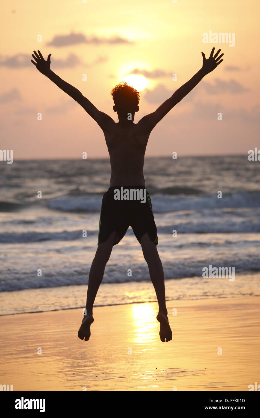 Kleiner Junge unter Hochsprung mit weit geöffneten Händen am Meeresstrand, Velagar, Shiroda, Sindhudurga, Maharashtra, Indien Herr #468 Stockfoto