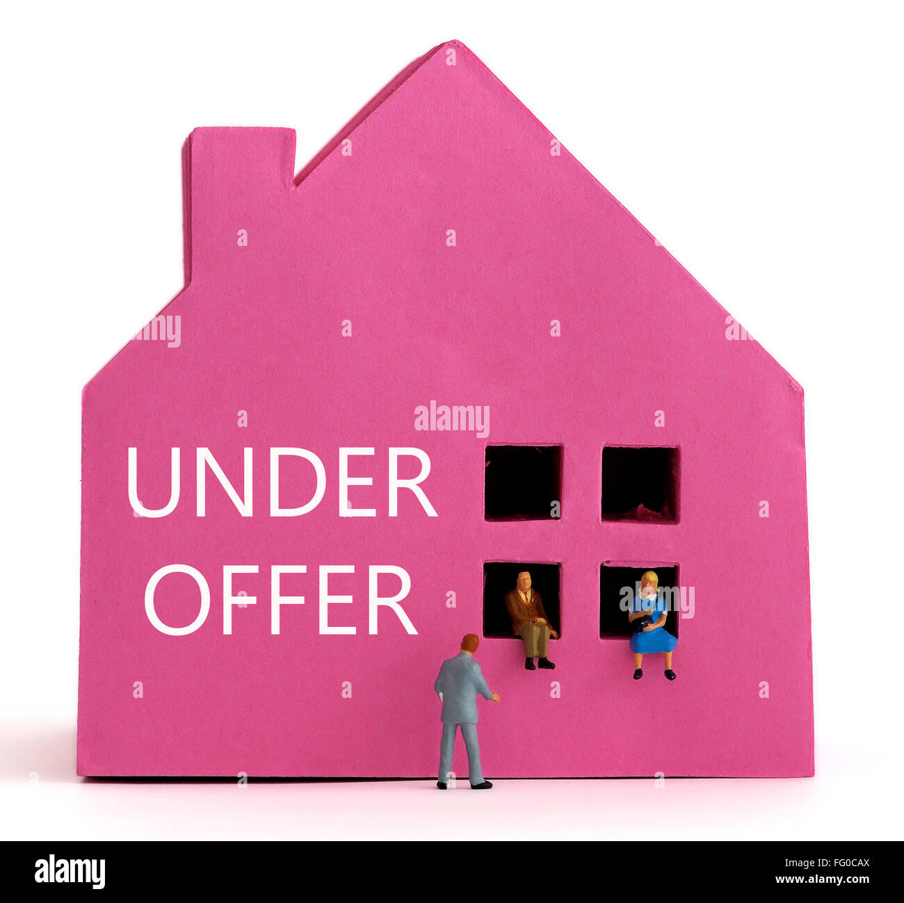 Ein rosa Papier-Haus und ein paar sitzen in den Fenstern mit einem Immobilienmakler in einem Anzug. Haus Kauf-Konzept. Stockfoto