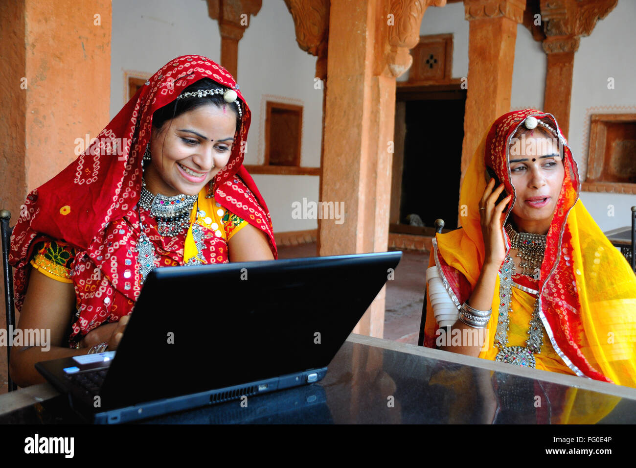Rajasthani-Dame auf der Suche am Laptop ein weiteres Gespräch auf Mobile; Rajasthan; Indien Herr # 769; 769 C Stockfoto