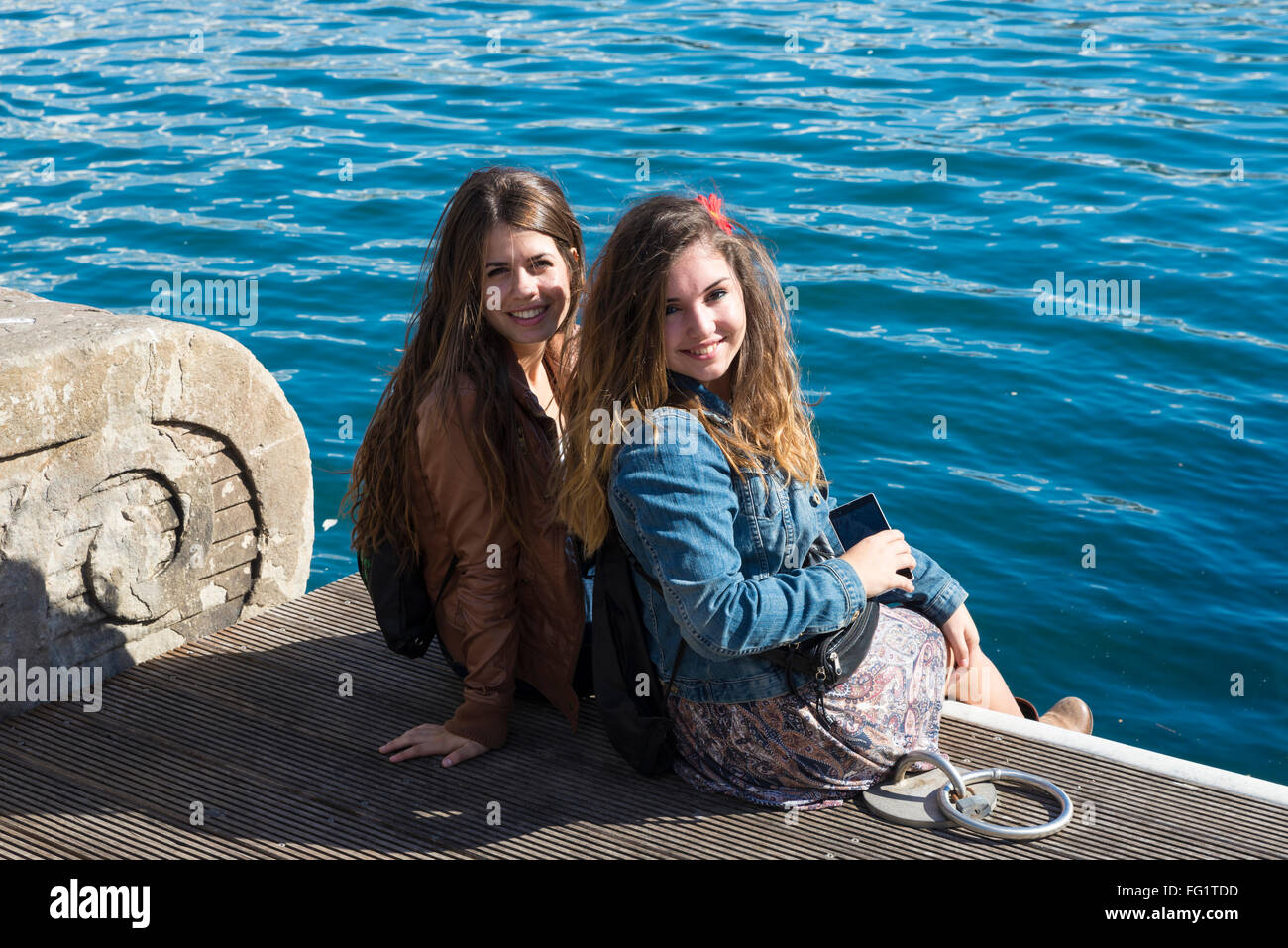 Zwei hübsche Mädchen sitzen in der Nähe des Meeres auf der Treppe von einem Pier in Barcelona, Katalonien, Spanien Stockfoto