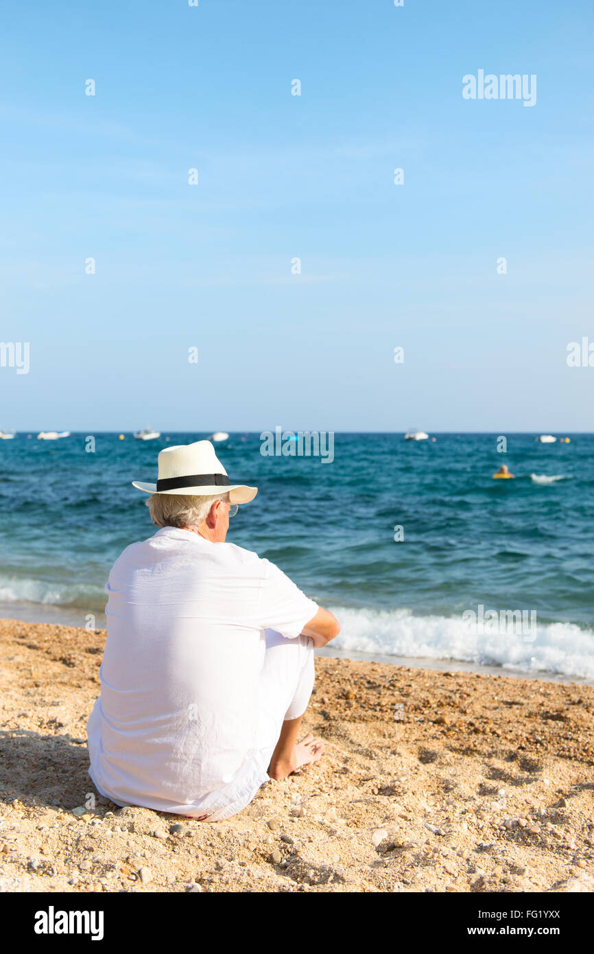 Ältere Mann im weißen Anzug sitzt am Strand Stockfoto