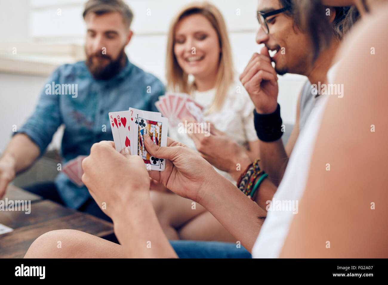 Gruppe von Freunden zusammensitzen Spielkarten. Spielkarten in Händen einer Frau während einer Party im Mittelpunkt. Stockfoto