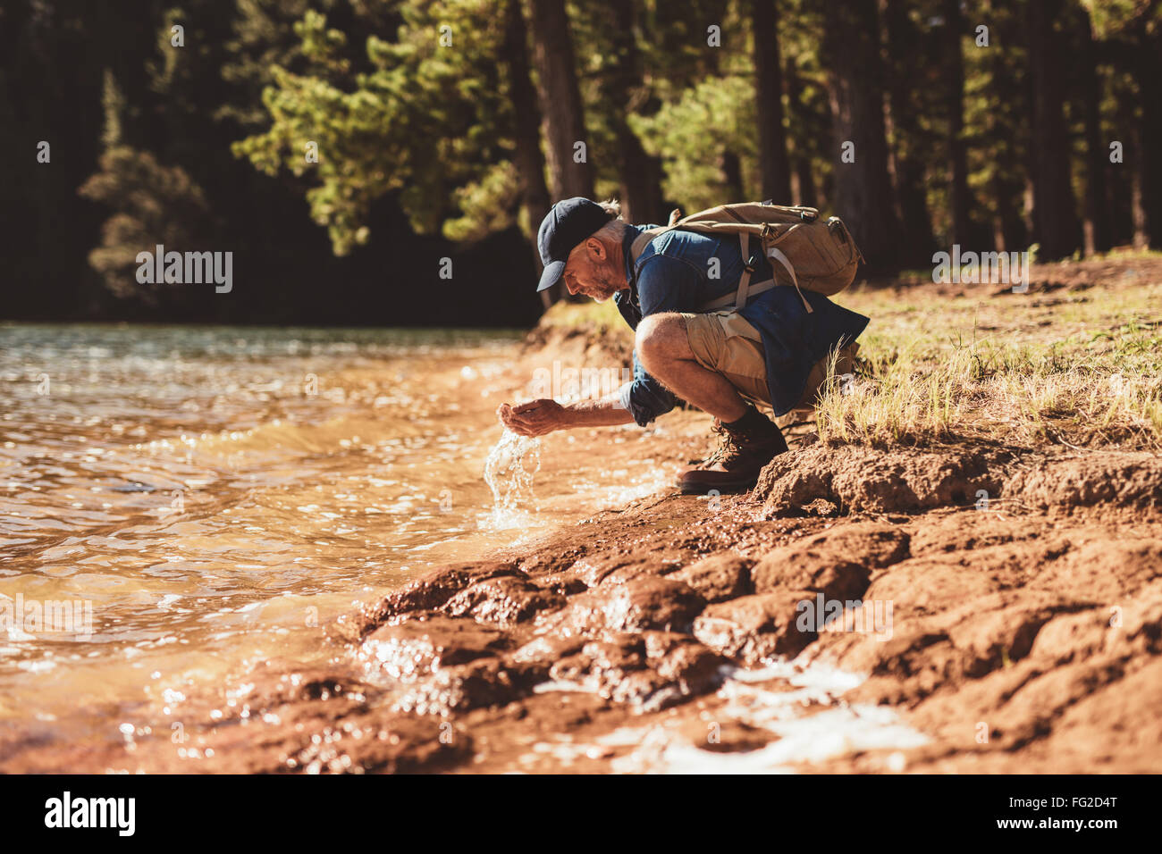 Porträt von reifer Mann sein Gesicht mit Wasser waschen. Senior kaukasischen Mann waschen Gesicht vom Wasser des Sees an einem Sommertag. Stockfoto