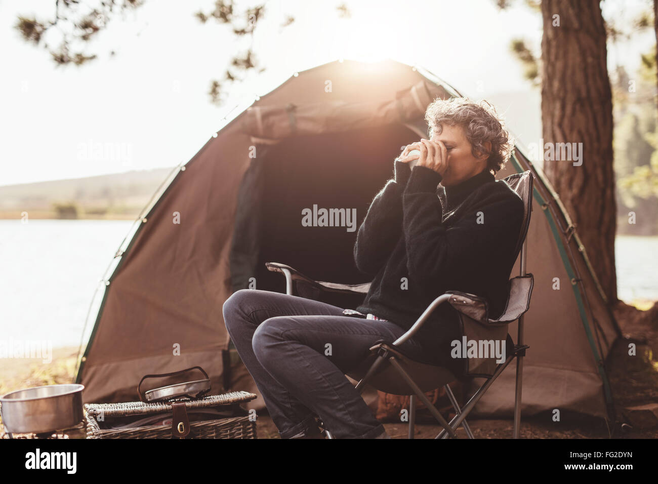 Porträt von Reife Frau sitzen auf Stuhl auf Campingplatz Kaffee trinken. Kaukasische Frau camping in der Natur am Sommertag. Stockfoto