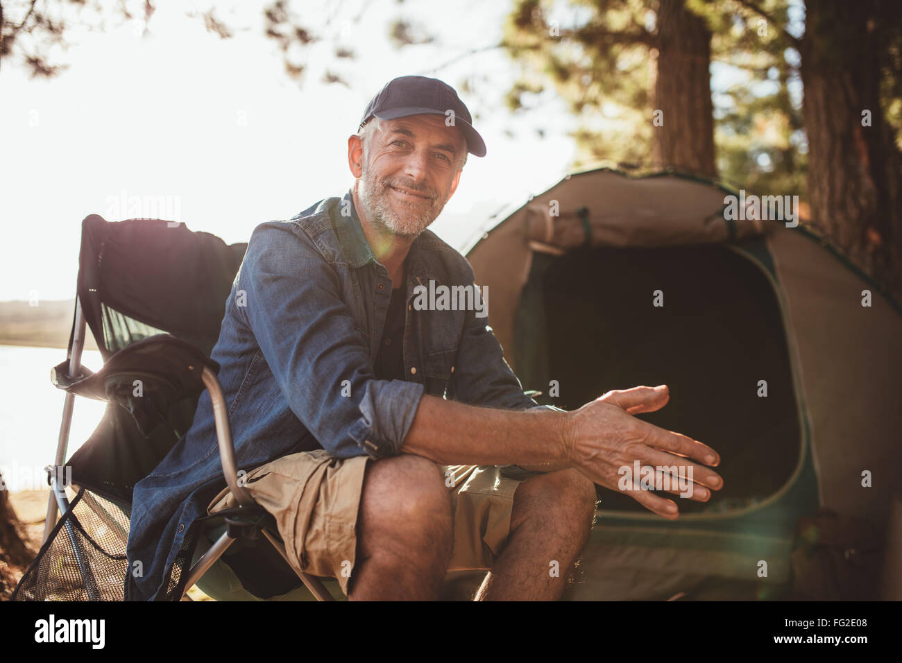 Porträt einer glücklich reifer Mann sitzt vor einem Zelt und Blick in die Kamera. Senior kaukasischen Mann am Campingplatz. Stockfoto