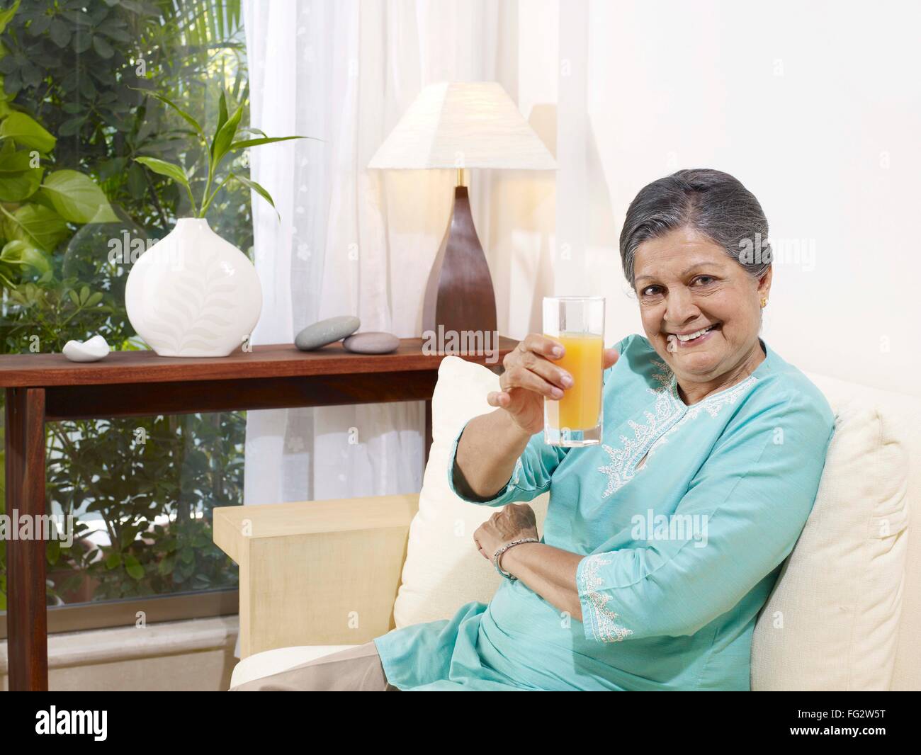 Alte Dame zeigt Glas Saft auf Sofa Herr #702S Stockfoto
