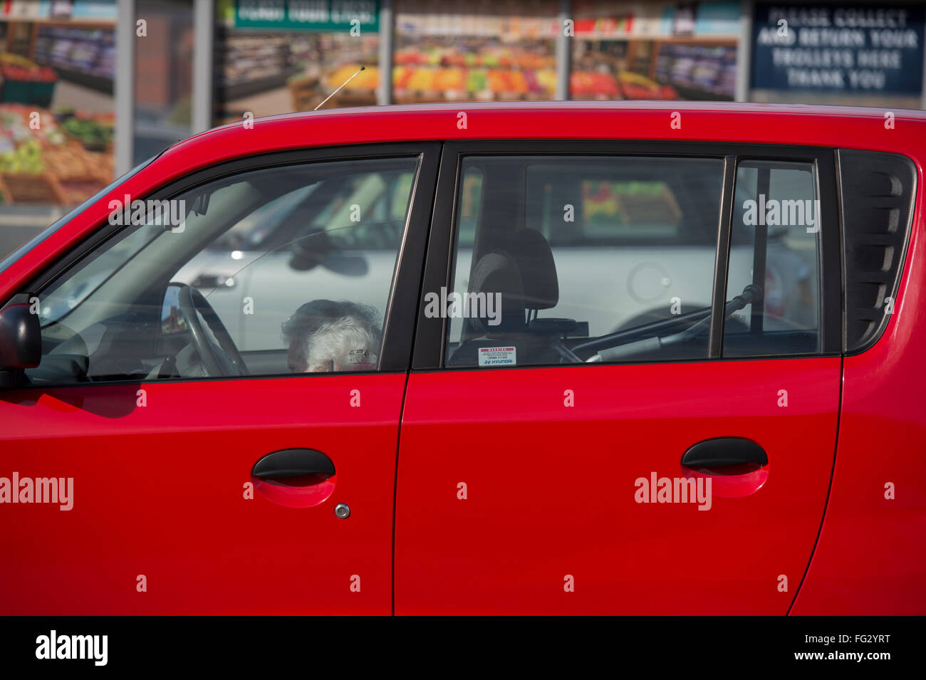 Kleine, ältere, grauhaarige Dame, sitzt auf dem Beifahrersitz ein rotes Auto, so klein ist sie kaum sichtbar über der Tür - England, GB, UK. Stockfoto