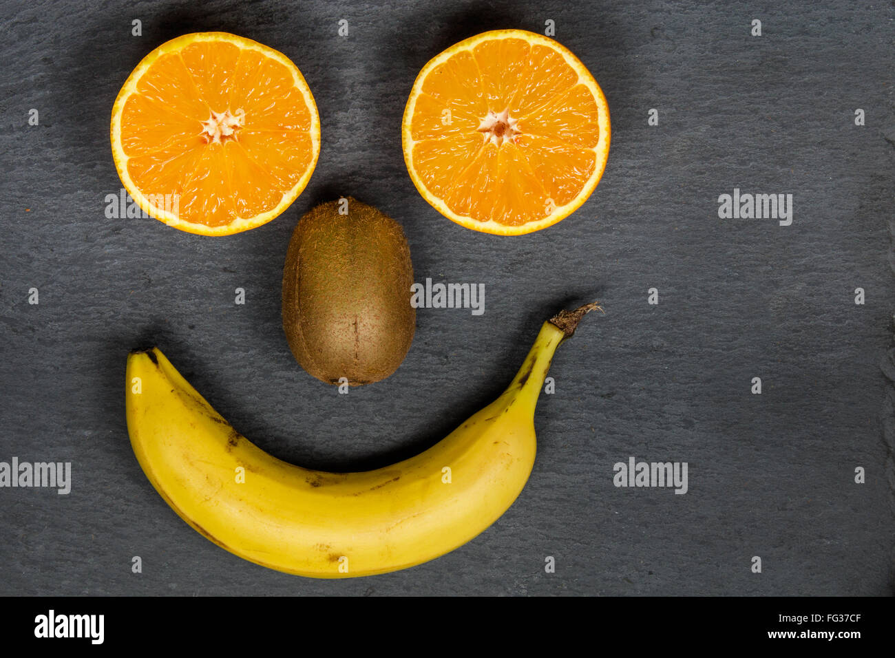 Früchte zu essen machen Sie Lächeln wie dieses glückliches Gesicht. Essen Sie Bio, bleiben Sie gesund zu. Essen-Platte mit Früchten auf einem dunklen Hintergrund. Stockfoto