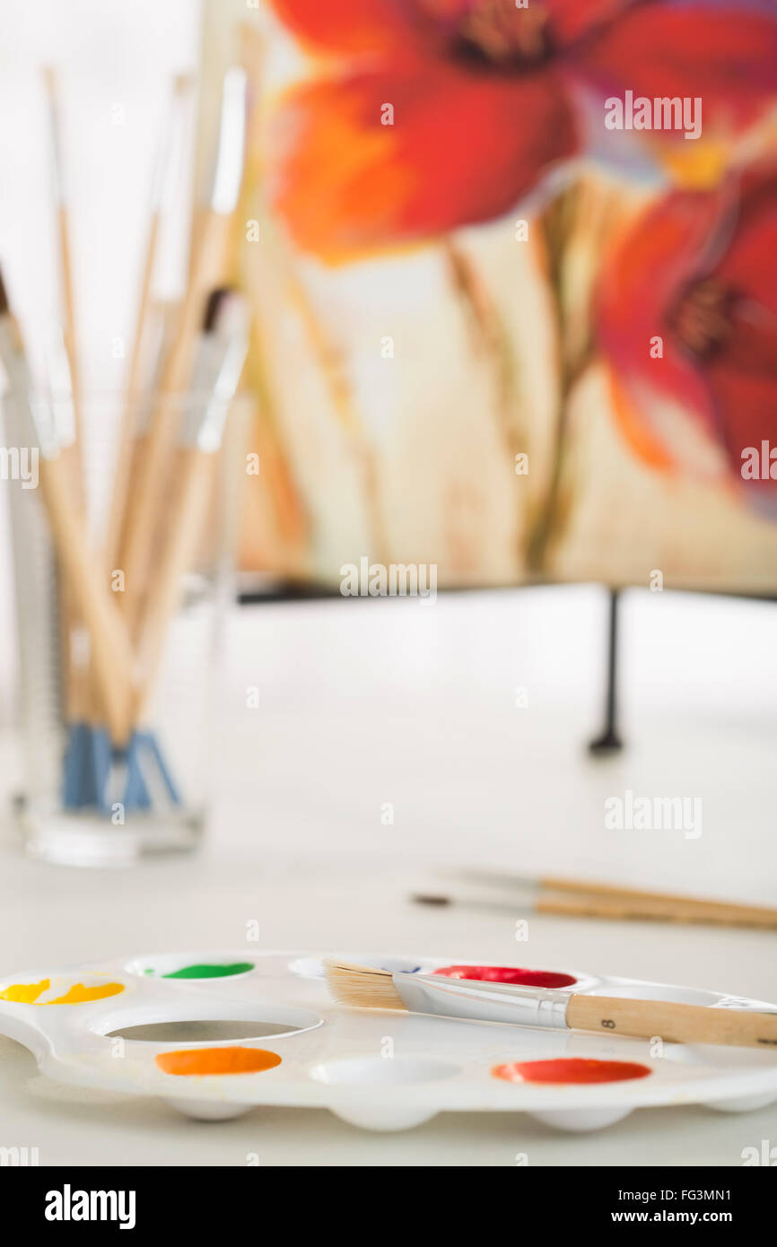 Palette und Pinsel in Kunstatelier mit Malerei im Hintergrund Stockfoto