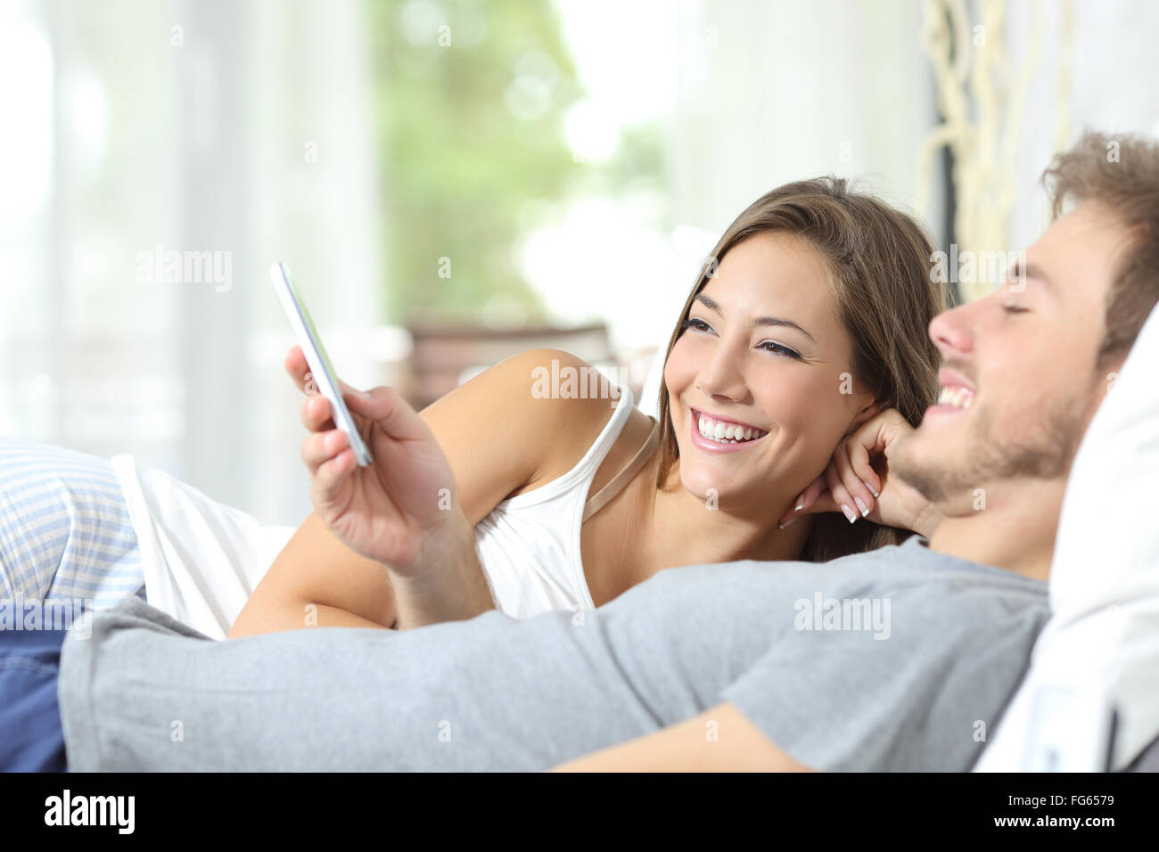 Glückliches Paar teilen ein intelligentes Telefon beobachten Medieninhalte auf dem Bett Stockfoto