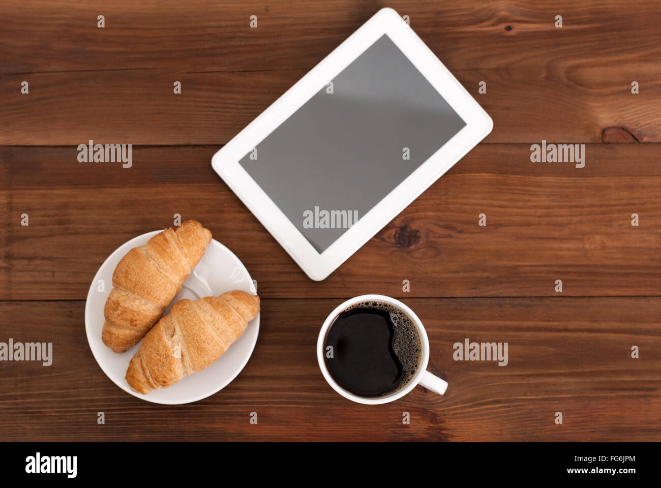 Kaffee-digital-Tablette und Croissants auf einem Holztisch. Stockfoto