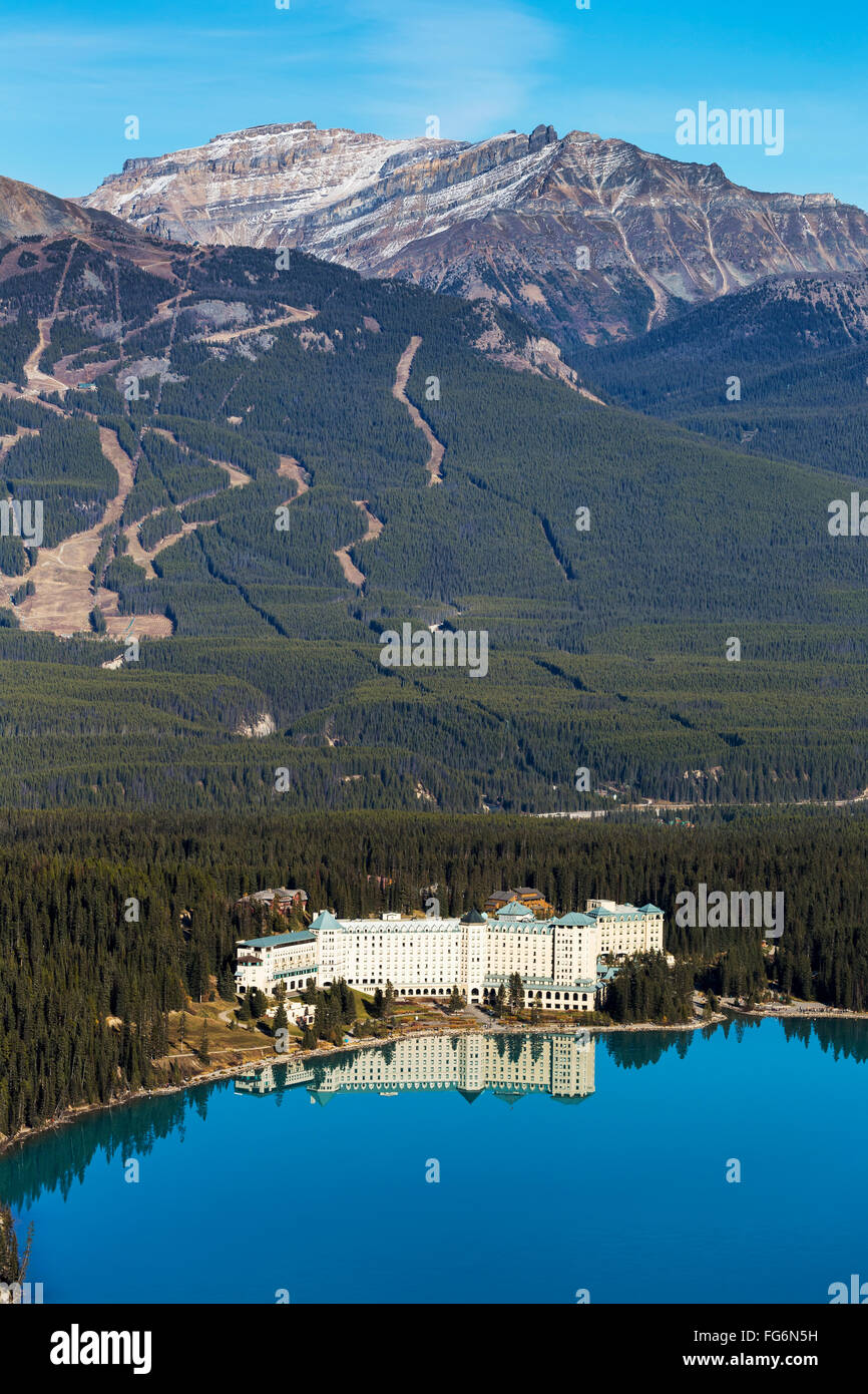Chateau Lake Louise spiegelt sich in der ruhigen intensiven blauen Bergsee mit Ski-Hügel läuft im Hintergrund und blauem Himmel Stockfoto