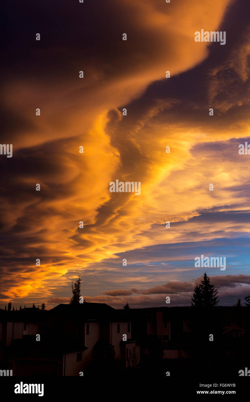 Dramatische bunten Wolken bei Sonnenuntergang mit interessanten Formationen und einige blaue Himmel mit Häusern in einer Nachbarschaft; Calgary, Alberta, Kanada Stockfoto