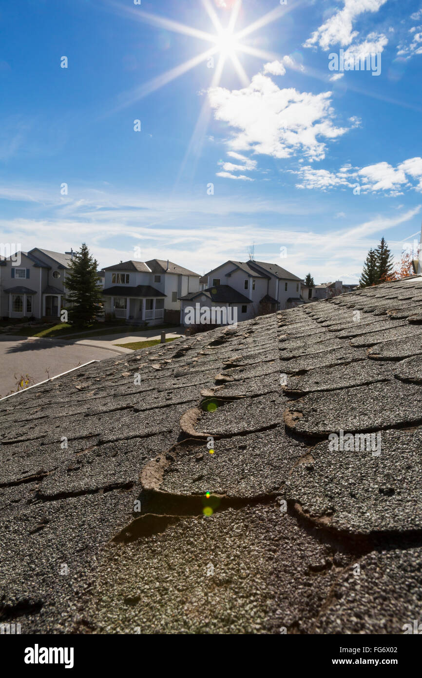 Nahaufnahme von gut getragen abgerundetes Dachschindeln mit Nachbarschaft Häuser, Burst Sonne, blauer Himmel und Wolken im Hintergrund; Calgary, Alberta, Kanada Stockfoto