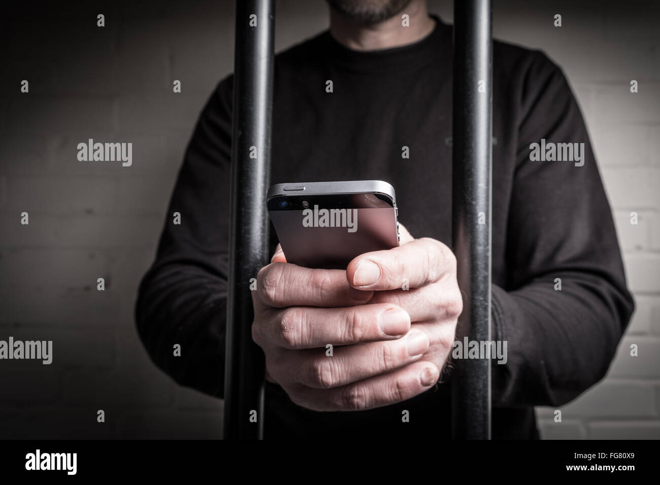 Ein Häftling im Gefängnis mit einem Mobiltelefon hinter Gittern in einer Zelle Stockfoto
