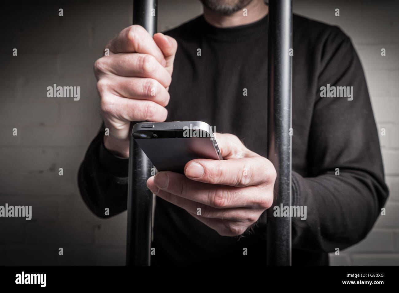 Ein Häftling im Gefängnis mit einem Mobiltelefon hinter Gittern in einer Zelle Stockfoto