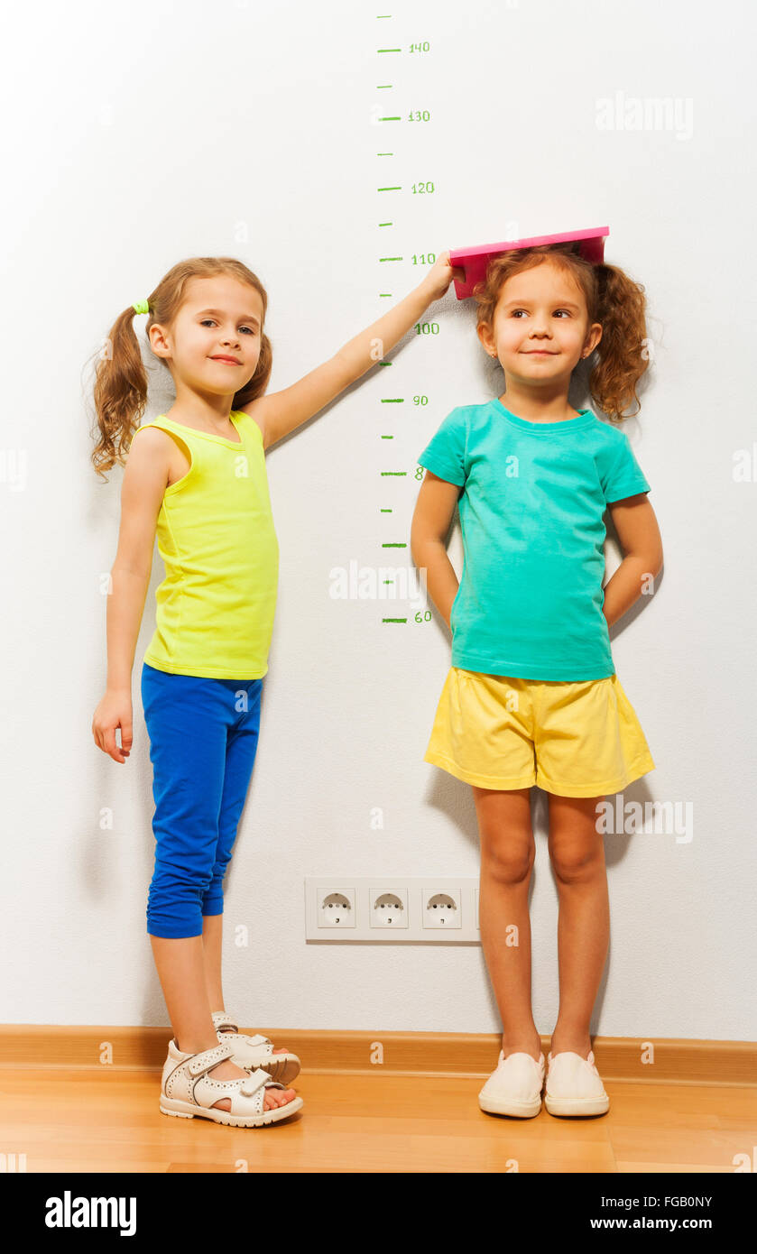 Kleine Mädchen helfen Freund Höhe im Maßstab messen Stockfoto