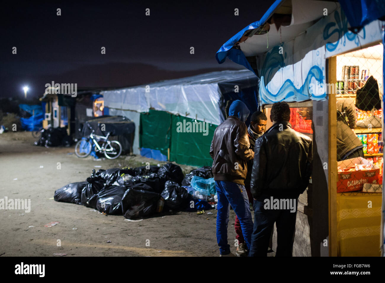 Syrische Männer kaufen Lebensmittel aus einem afghanischen Store in einer Straße in der Nacht. Müll im Hintergrund im Dschungel Flüchtlingslager, Calais. Stockfoto