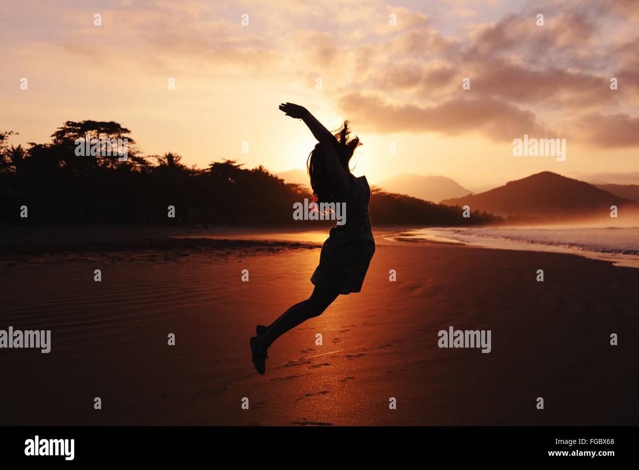 Seitenansicht der Silhouette Frau mit erhobenen Armen springen am Strand Stockfoto