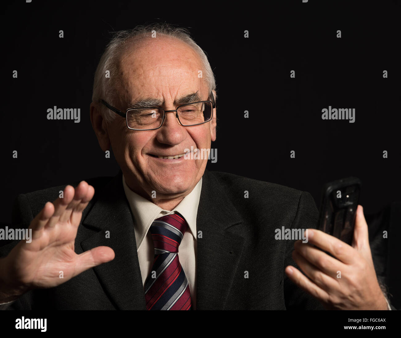 älteren Geschäftsmann, tragen Brillen auf schwarzem Hintergrund, Smartphone nutzt, hat video-chat Stockfoto
