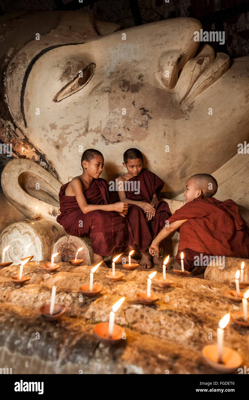Junge Mönche sitzen vor einem alten Buddha-Statue beleuchtet mit Kerzen. Stockfoto