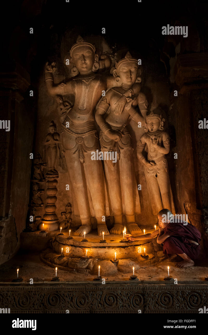 Junger Mönch Anzünden von Kerzen vor der alten buddhistischen Statue. Stockfoto