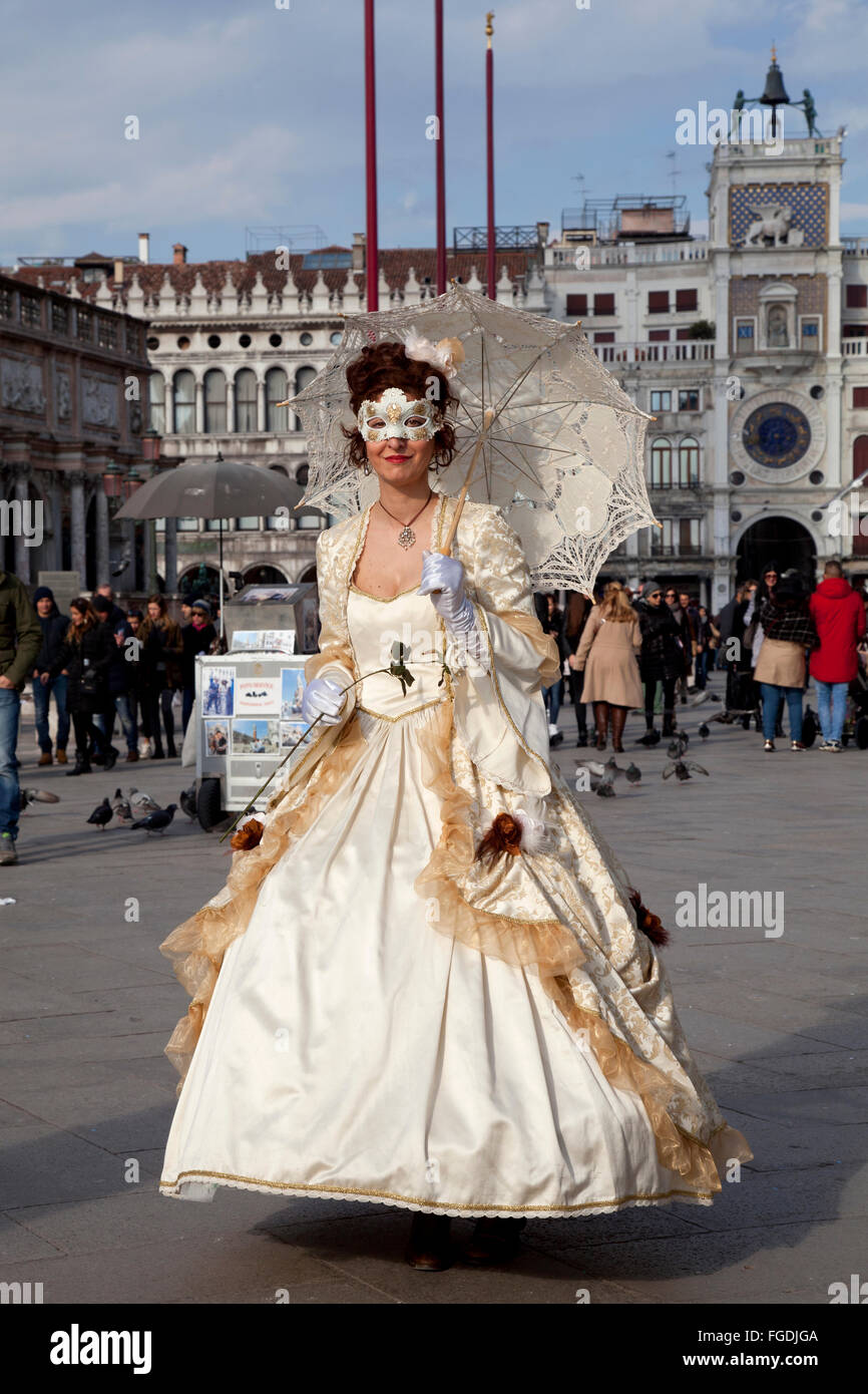 Maskierte Frau in Creme historischen Kleid mit Sonnenschirm feiert Karneval in Venedig, Markusplatz entfernt mit Torre Orologio auf der Rückseite Stockfoto