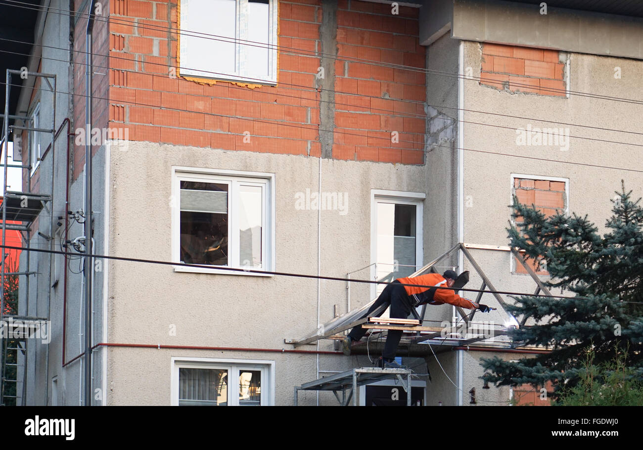 Mann Schweißen Dachkonstruktion dabei in eine gefährliche Position. Er hat keine entsprechende Ausrüstung oder Schutzeinrichtungen. Stockfoto