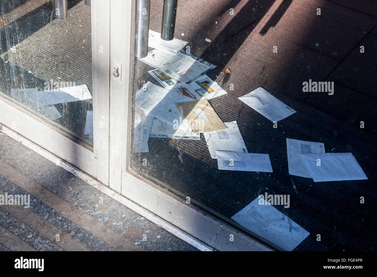 Viele ungeöffnete Mail auf dem Boden durch eine geschlossene Glastür Shop gesehen. Konzept einer Store, oder aus dem Geschäft gegangen, England, Großbritannien Stockfoto