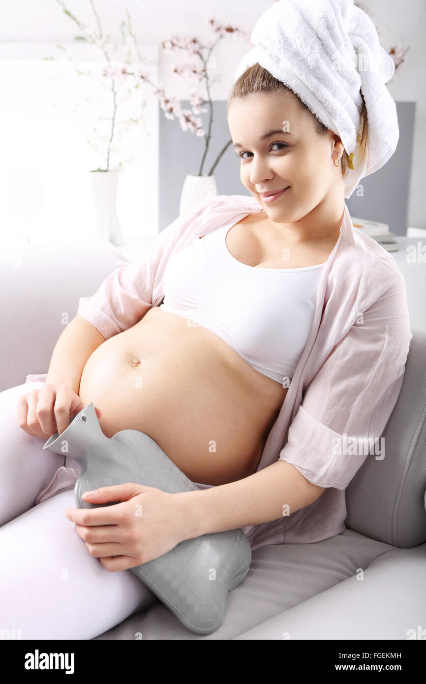 Grippe schwanger. Symptome der Schwangerschaft. Schwangere Frau erwärmt sich eine Wärmflasche auf dem Sofa ausruhen Stockfoto