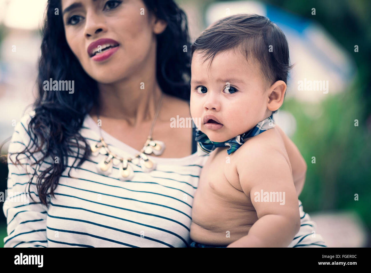 Hispanische Mutter mit ihrem männlichen Baby auf dem Arm. Der junge sucht direkt in die Kamera. Stockfoto