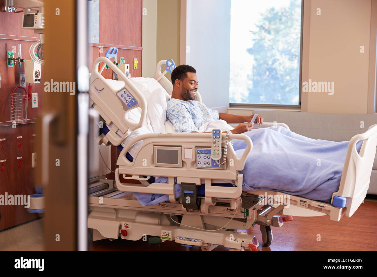 Männliche Patienten im Krankenhausbett mit Handy Stockfoto