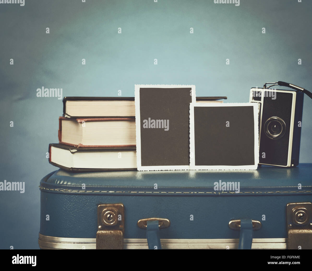 Alte Fotografien, eine Kamera und Bücher stehen ganz oben auf einem Vintage Koffer mit einem blauen Hintergrund für ein Speicherkonzept Stockfoto