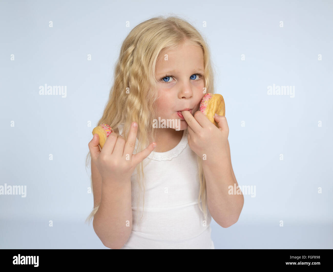 Junges Mädchen mit langen blonden Haaren Essen Donuts und leckte ihre Finger Stockfoto