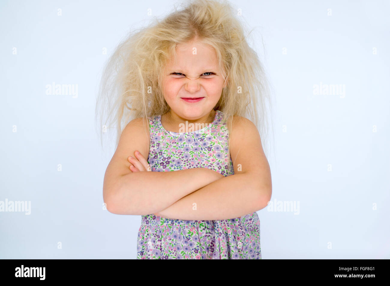 Junges Mädchen mit chaotisch blonde Haare mit verschränkten Armen und einem frechen Grinsen Stirnrunzeln Stockfoto