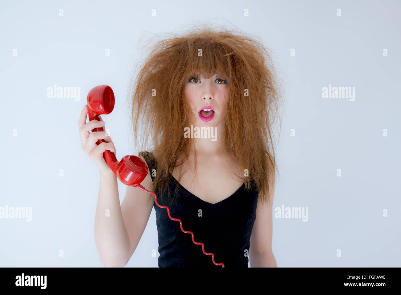 Frau mit strubbeligem Haar hält ein rotes Retro-Telefon mit einem Ausdruck der Verwirrung Stockfoto