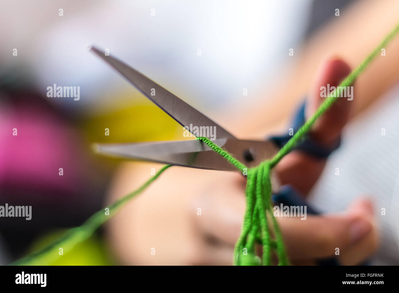 Hand hält eine Schere und schneiden grünen Faden Stockfoto