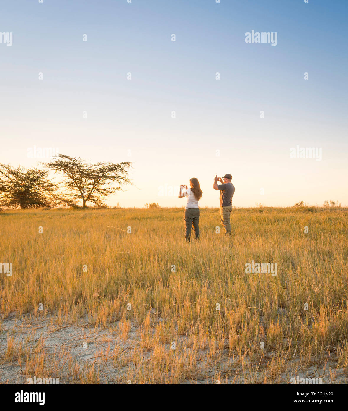 Ein junges Paar von Touristen fotografieren eines Afrikaners beim Sonnenuntergang auf Safari in die Makgadikgadi Salzpfannen, Botswana Stockfoto