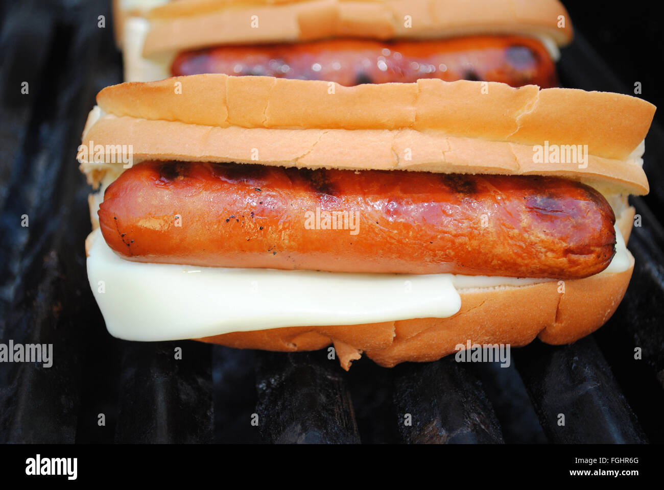 Schmelzende Käsescheiben auf Hot Dog Brötchen auf einem Grill Stockfoto