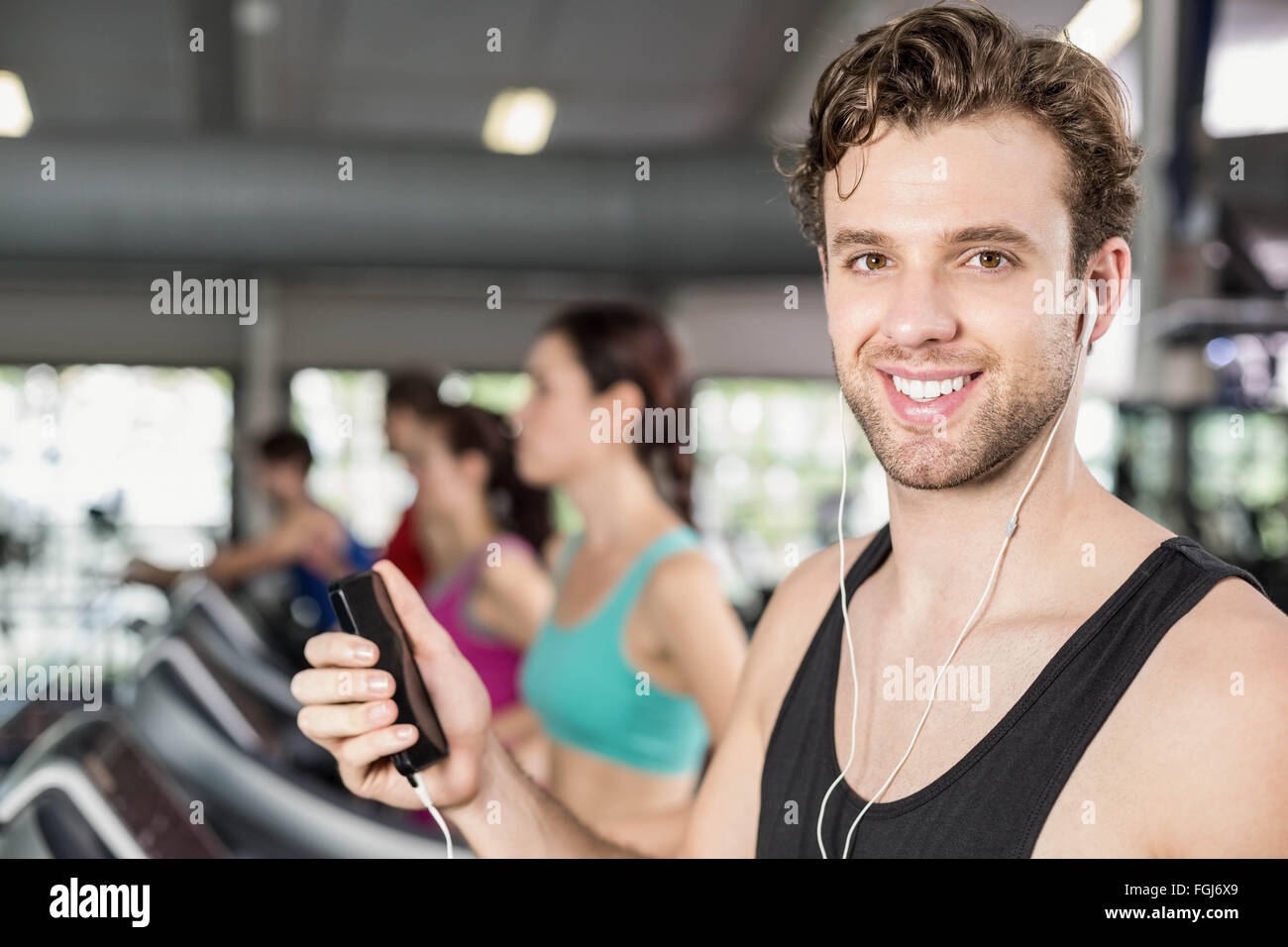 Lächelnde muskulöser Mann auf Laufband, Musik hören Stockfoto